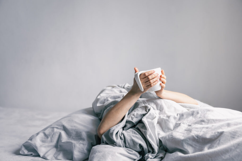 A woman's hand holds a cup of coffee while lying in bed.